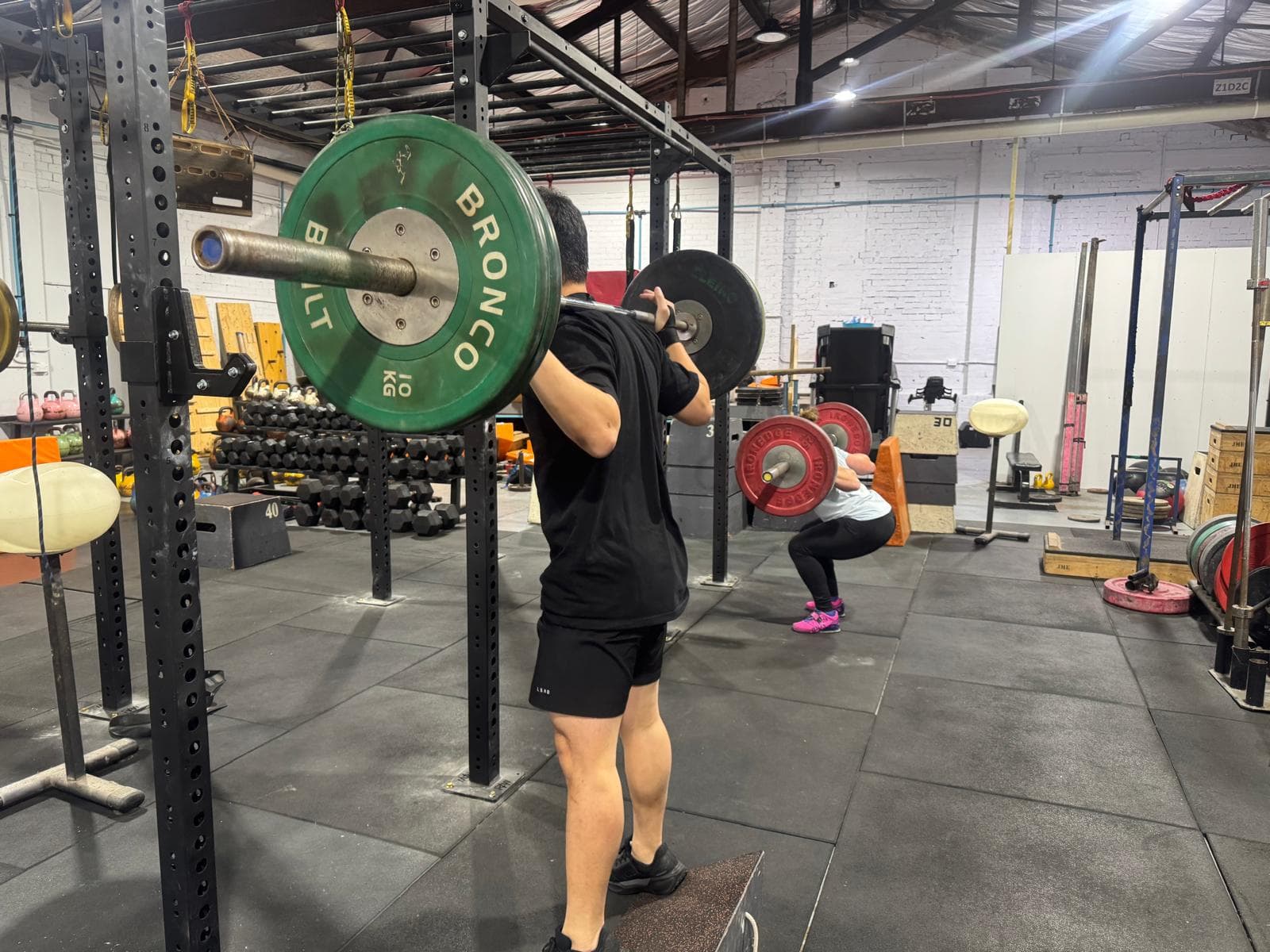 Two members squatting with loaded barbells on the gym floor
